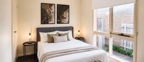 A hotel room with a large bed, two bedside tables, a window with a view, and a magazine on the bed.
