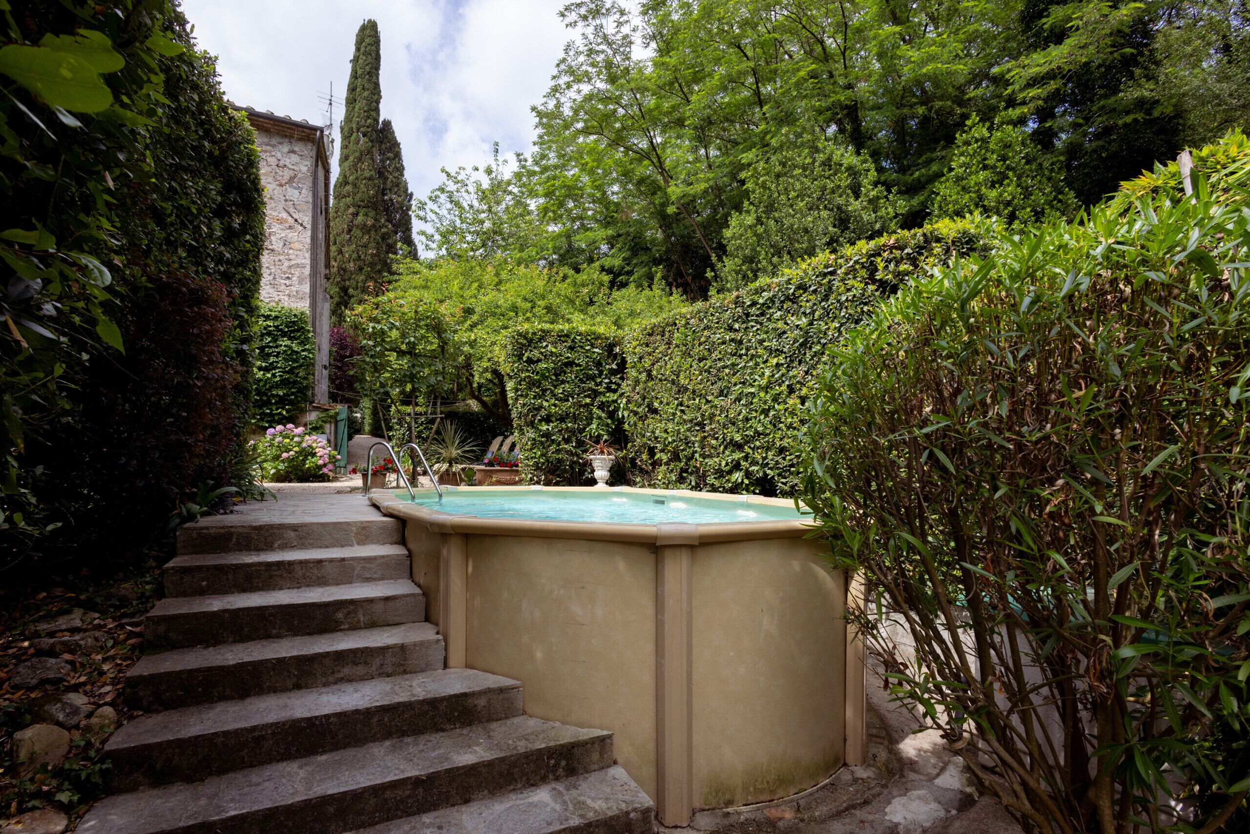 A stone staircase leading to a hot tub surrounded by lush greenery and a tall tree.
