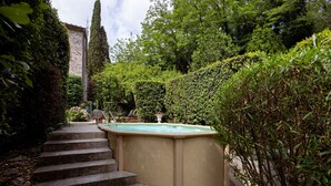 Un escalier en pierre mène à un bain à remous entouré d’une végétation luxuriante et bordé d’un grand arbre.