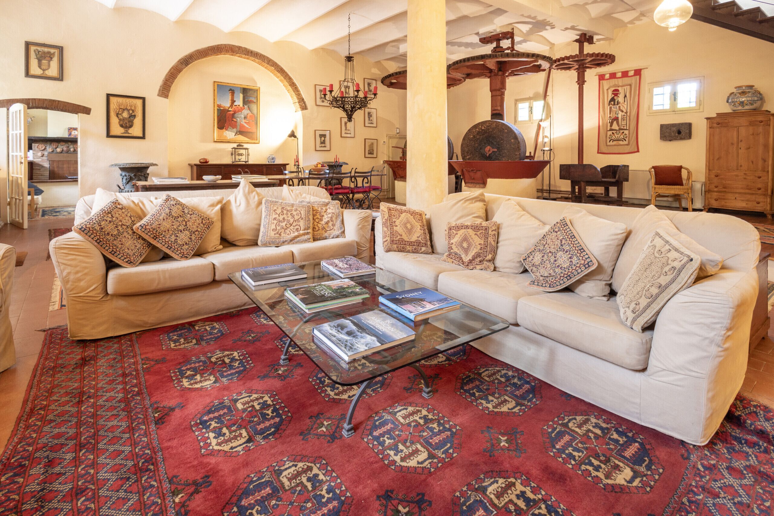 A spacious living room with two white sofas, a glass coffee table, and a red patterned rug.