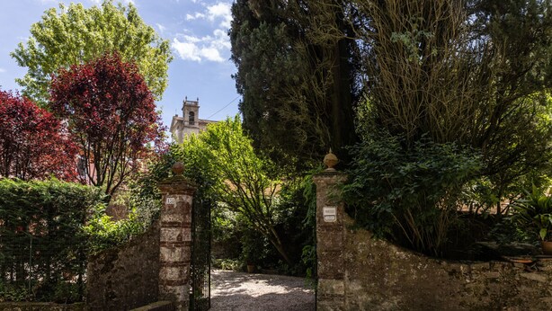 Un chemin de jardin qui mène à un bâtiment doté d’un mur en briques et d’un portail en métal.