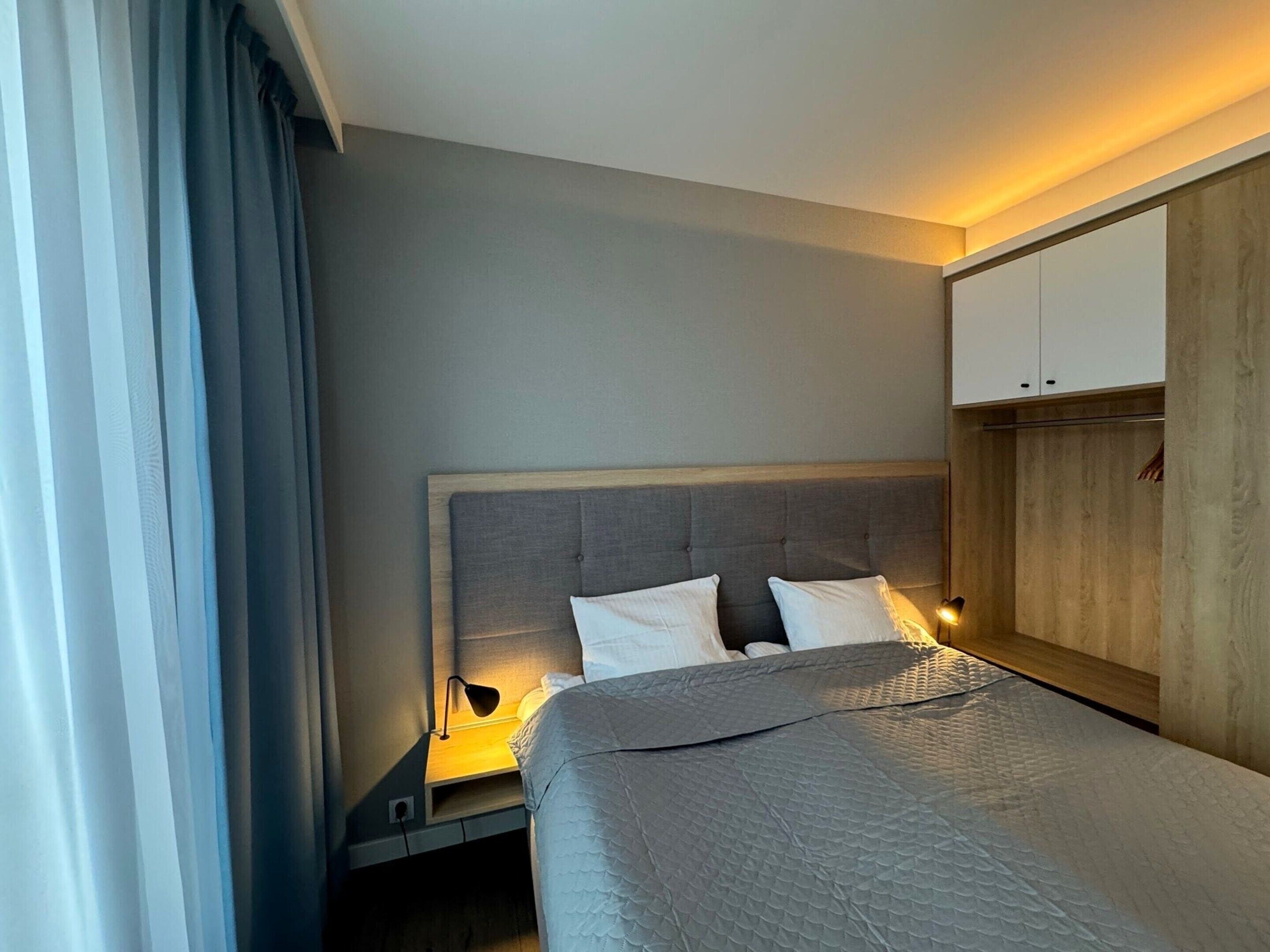A hotel room with a bed, bedside lamp, and a wardrobe.