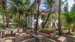 An outdoor seating area with wicker furniture, a glass-top table, and a thatched-roof building in the background. - Watano Beach House Spacious 7-bedroom house in awesome Diani perfect for groups (Diani)