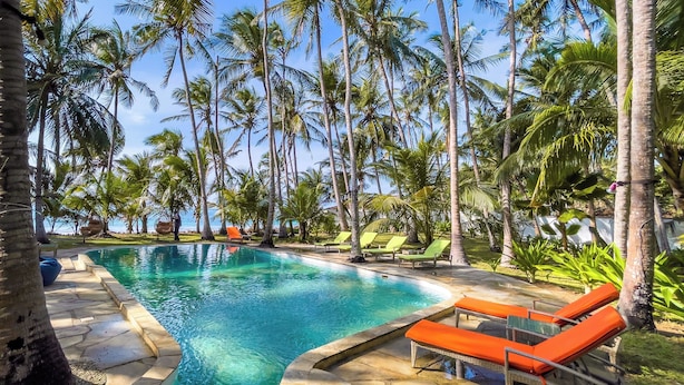 A swimming pool with lounge chairs, surrounded by palm trees. - Watano Beach House Spacious 7-bedroom house in awesome Diani perfect for groups (Diani)