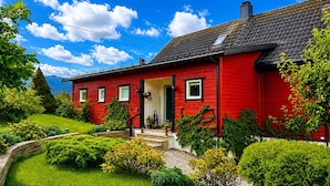 Una casa roja con techo negro, rodeada de vegetación y un cielo despejado.