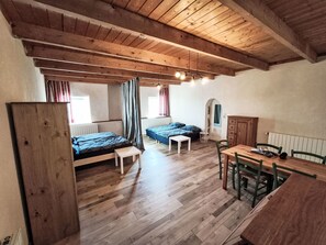 Een kamer met houten vloeren, een bed, een tafel met stoelen en een raam met gordijnen.