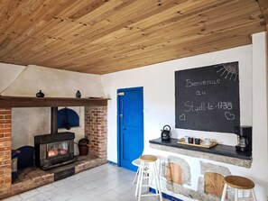 Een gezellige kamer met een schouw van baksteen, een blauwe deur en een schoolbord waarop 'Bienvenue au Stoddle 1739' staat.