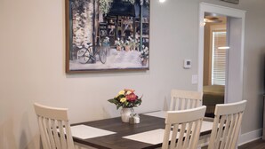 A dining area with a table set for four, a vase of flowers, and a painting on the wall. - Cozy 2-bedroom house nestled among the trees and surrounded by open space. (Eastman)
