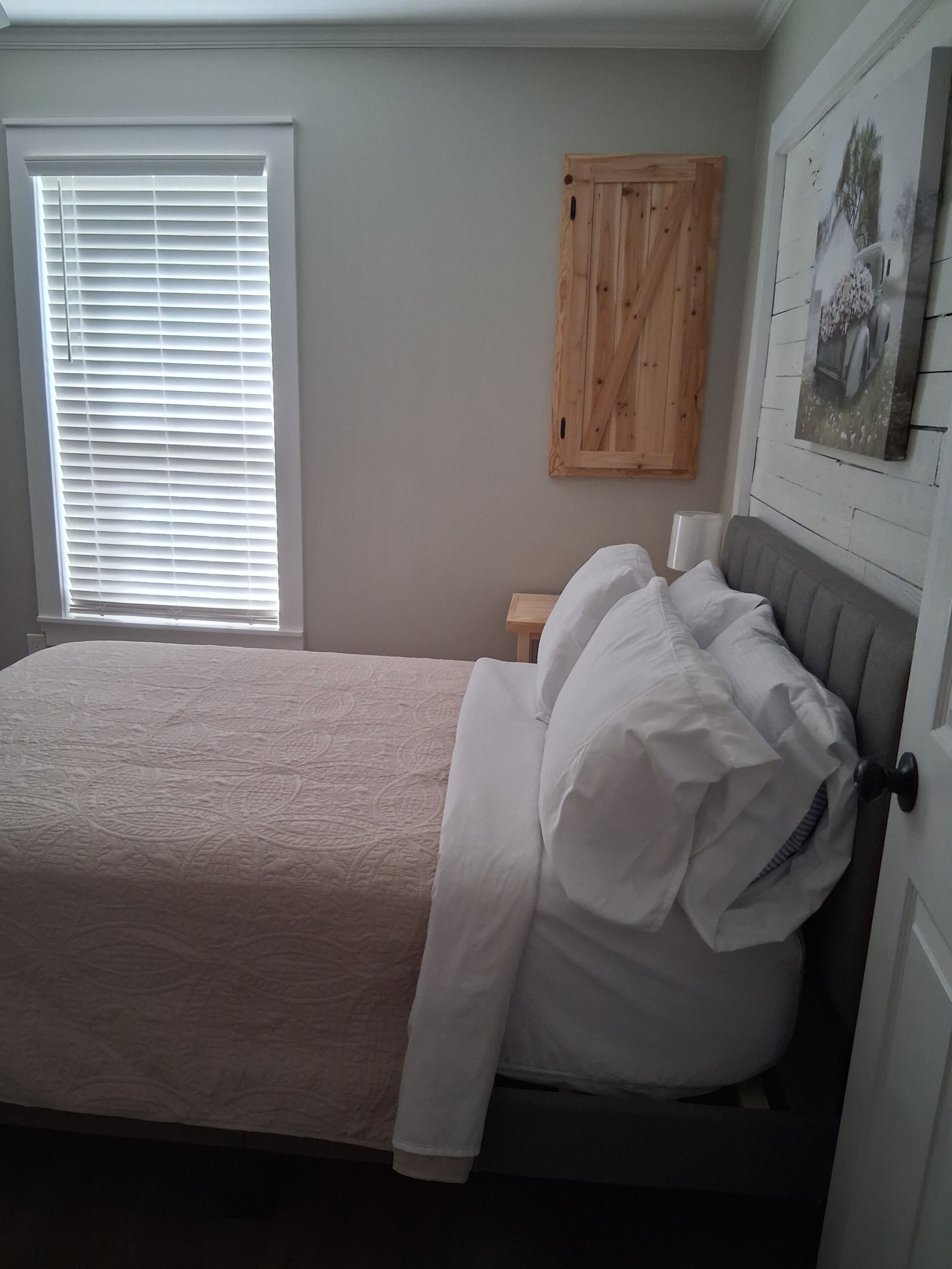 A bedroom with a bed, a window with blinds, a wooden cabinet, and a wall-mounted picture.