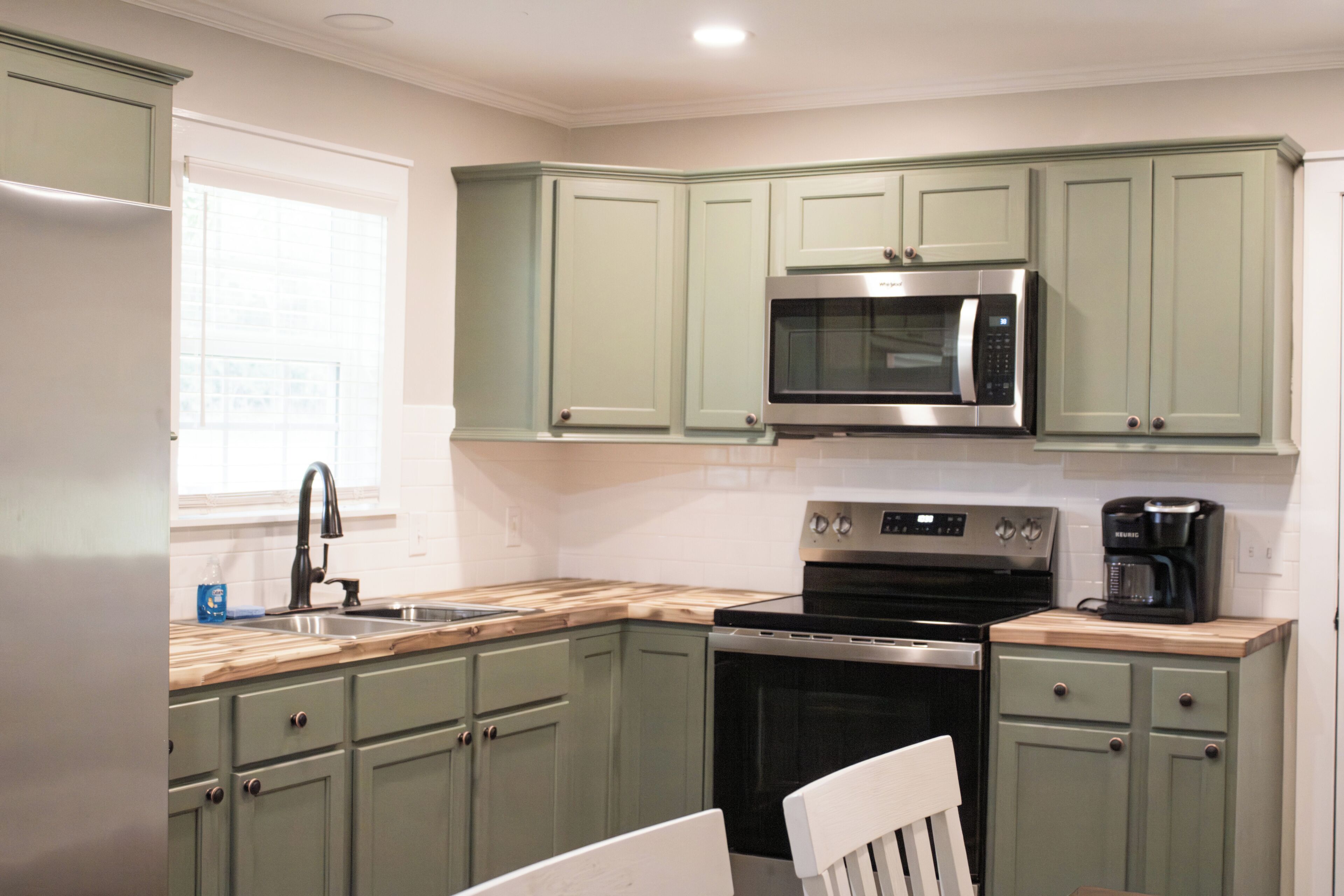 A kitchen with green cabinets, a stainless steel microwave, an oven, and a coffee maker.