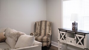 A room with a patterned armchair, a sofa with a leopard print throw, and a white cabinet with drawers. - Cozy 2-bedroom house nestled among the trees and surrounded by open space. (Eastman)