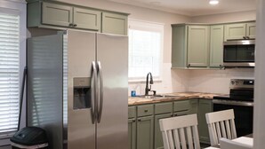 A kitchen with green cabinets, a stainless steel refrigerator, a microwave, and a sink. - Cozy 2-bedroom house nestled among the trees and surrounded by open space. (Eastman)