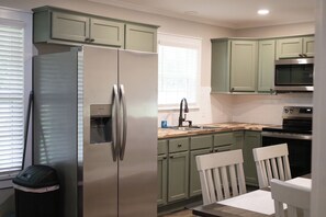 A kitchen with green cabinets, a stainless steel refrigerator, a microwave, and a sink.