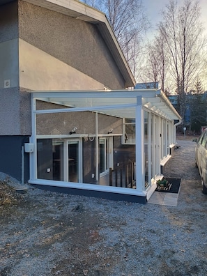 A modern building with a covered patio area, a car parked nearby, and a gravel driveway. - Spacious Luxury Apartment (Hameenlinna)