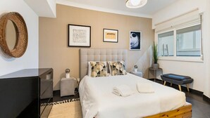 Een moderne slaapkamer met een bed, nachtkastjes, een spiegel en kunst aan de muur.