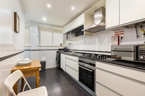 A compact kitchen with a stove, microwave, and oven. There is a dining table with chairs and a small window.