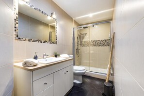 Un bagno moderno con doccia a vetro, lavandino bianco e uno specchio grande.