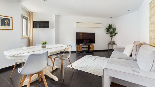 Een moderne woonkamer met een eethoek, een flatscreen-televisie, een bank en een potplant.