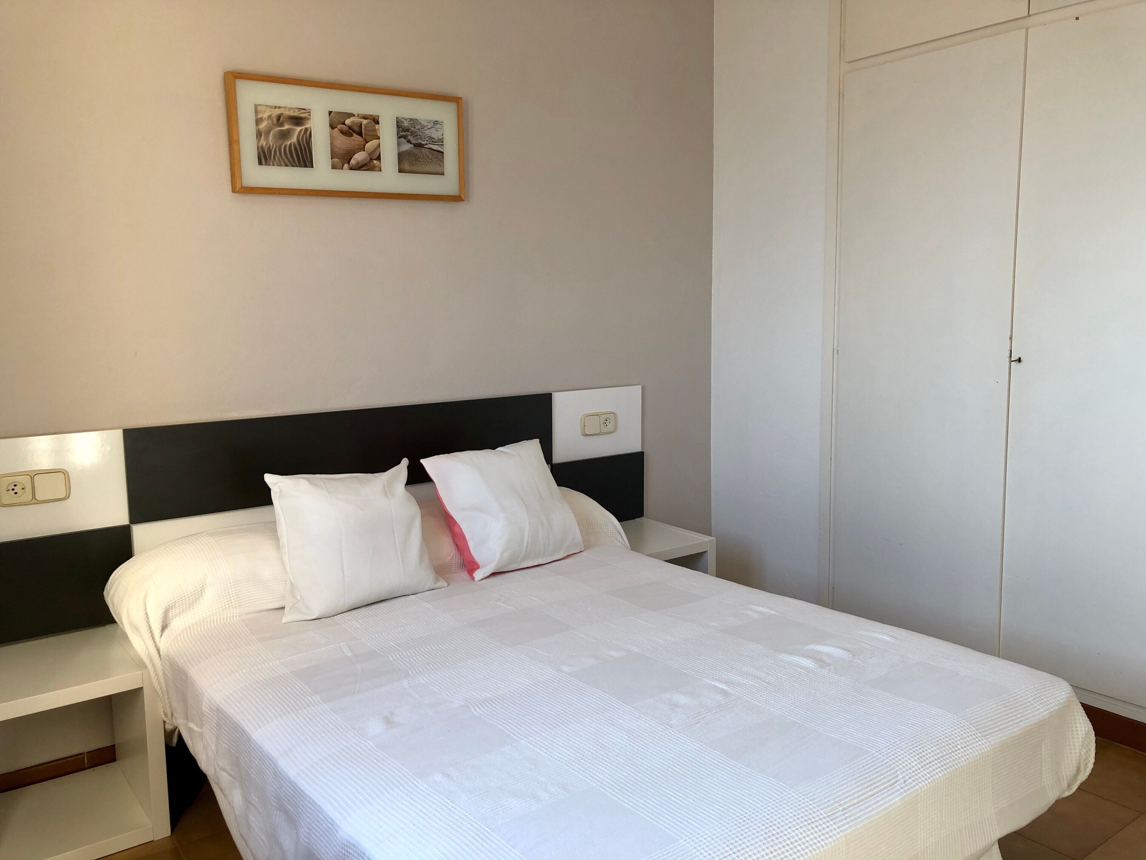 A neatly made bed with white bedding, a black headboard, and a small bedside table with a lamp.
