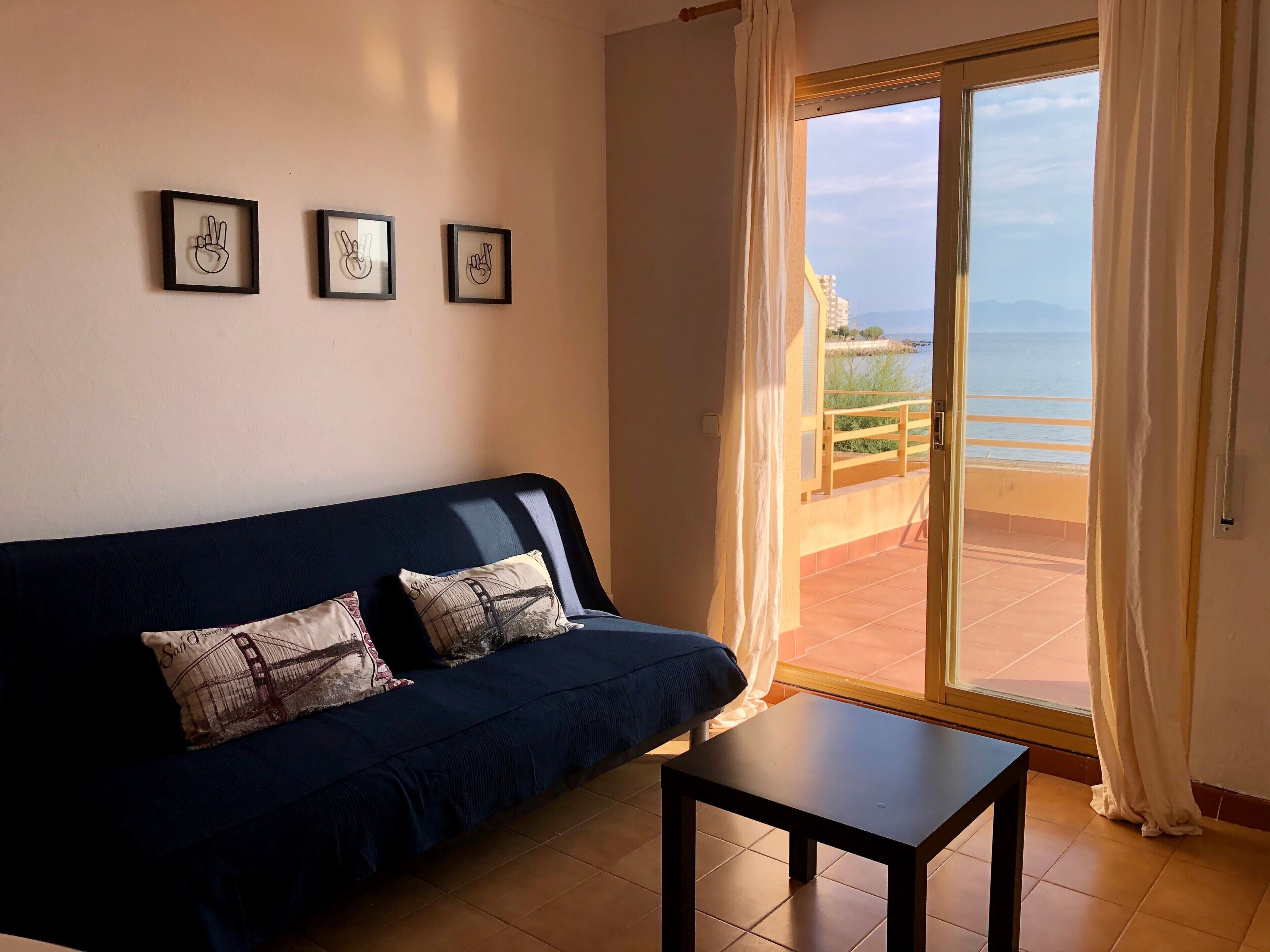 A room with a dark blue sofa, a small table, and three framed pictures on the wall.