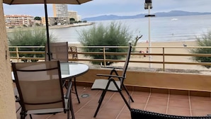 Eine Terrasse mit Tisch und Stühlen mit Blick auf einen Strand und ein Gewässer.