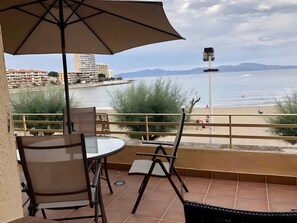 Una terraza con una mesa y sillas, con vista a una playa y una extensión de agua.