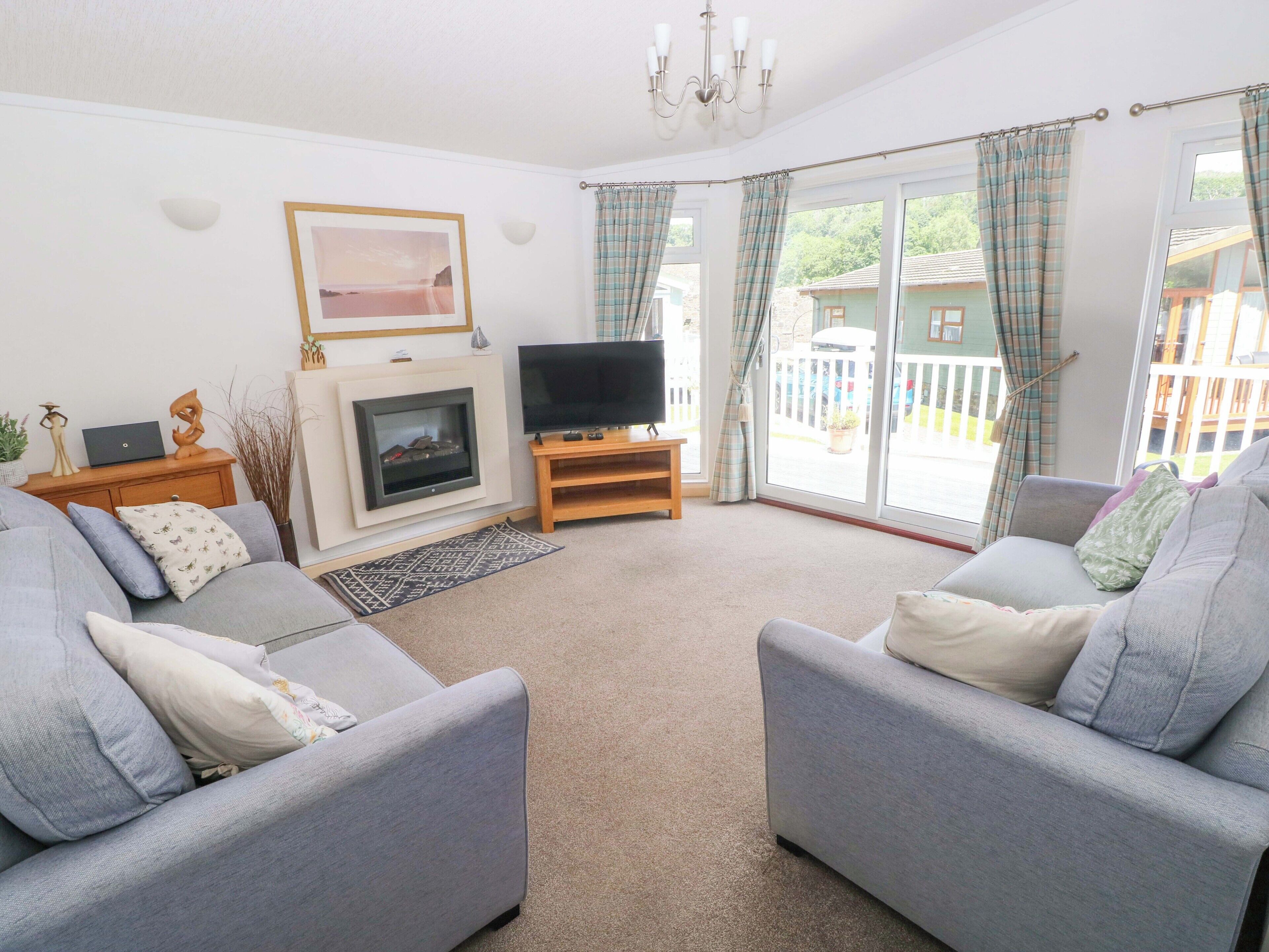 A living room with two grey sofas, a flat-screen TV, a fireplace, and a large window with curtains.
