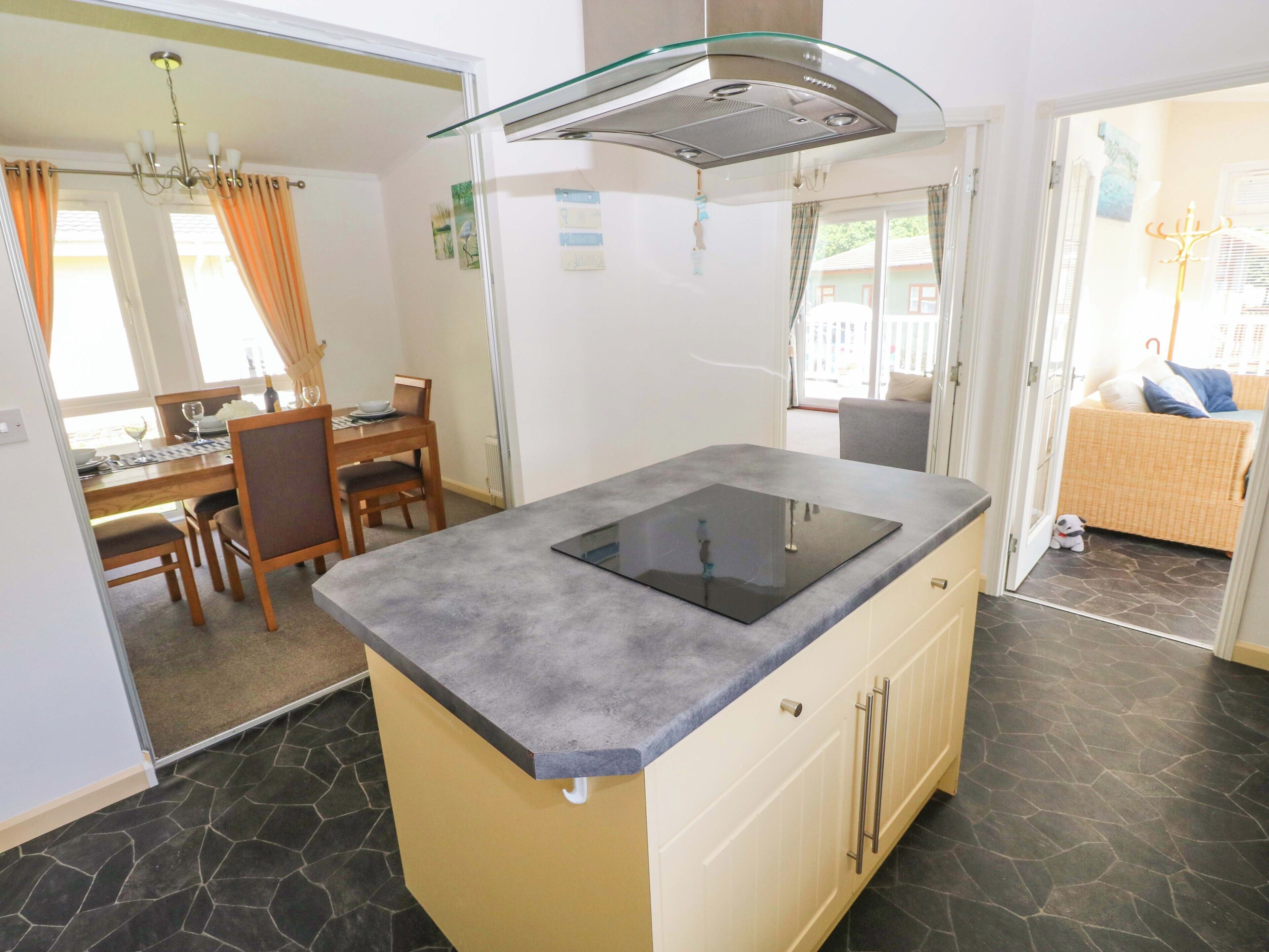 Une cuisine moderne dotée d’un îlot central, d’un coin repas avec une table et des chaises, et offrant une vue sur l’extérieur.