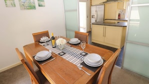 Comedor con mesa de madera dispuesta para cuatro personas, cocina al fondo y decoración en las paredes.