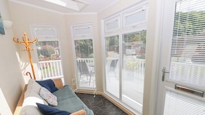 Habitación iluminada por el sol con un sofá de mimbre, un perchero metálico y vistas a un patio con mobiliario exterior.