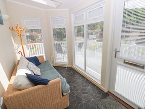 A sunlit room with a wicker sofa, a metal coat rack, and a view of a patio with outdoor furniture.