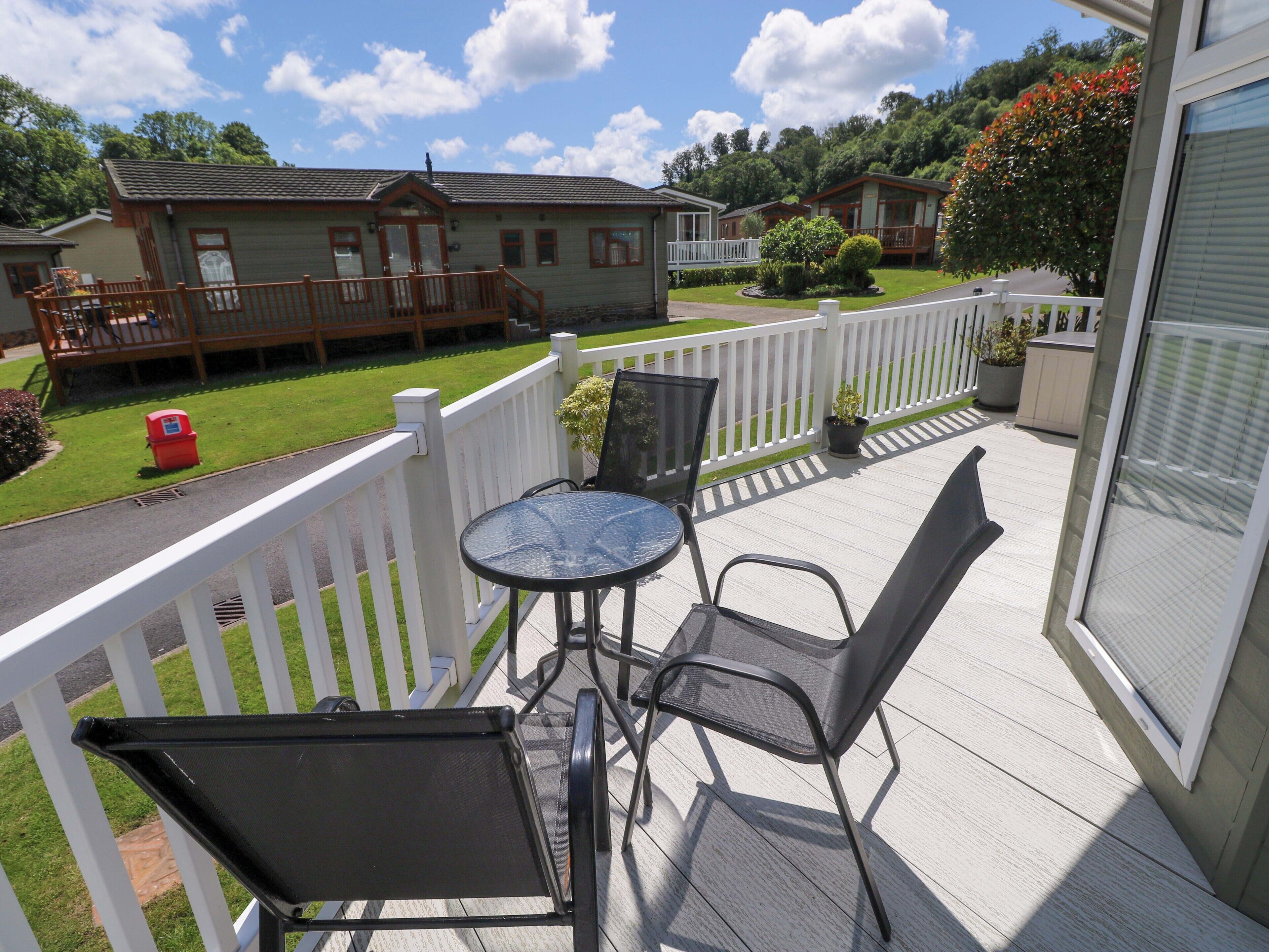 A balcony with a table and chairs, white railings, and a view of nearby houses.