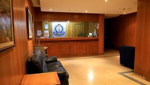 A reception area with a wooden reception desk, a leather sofa, and a small table. - Braga Restaurante e Residencial (Lourinha)