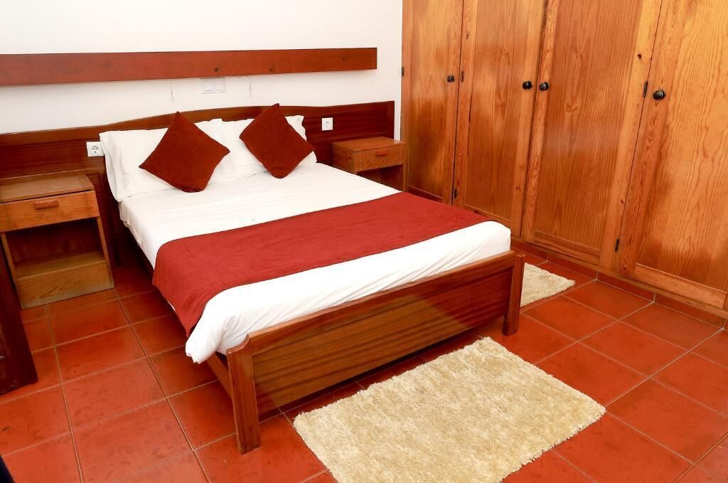 Un dormitorio con una cama de madera, una mesita de noche, un armario y una alfombra roja.