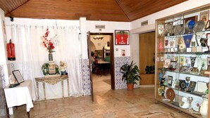 A room with a tiled floor, a table with a vase of flowers, a framed picture, and a glass display case with various items. - Braga Restaurante e Residencial (Lourinha)