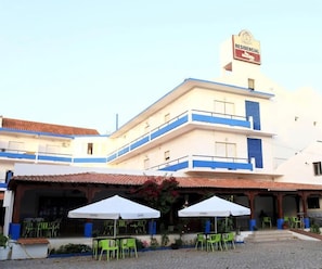 A building with a sign reading 'RESIDENCIAL' and a covered outdoor seating area with green chairs and white umbrellas. - Braga Restaurante e Residencial (Lourinha)