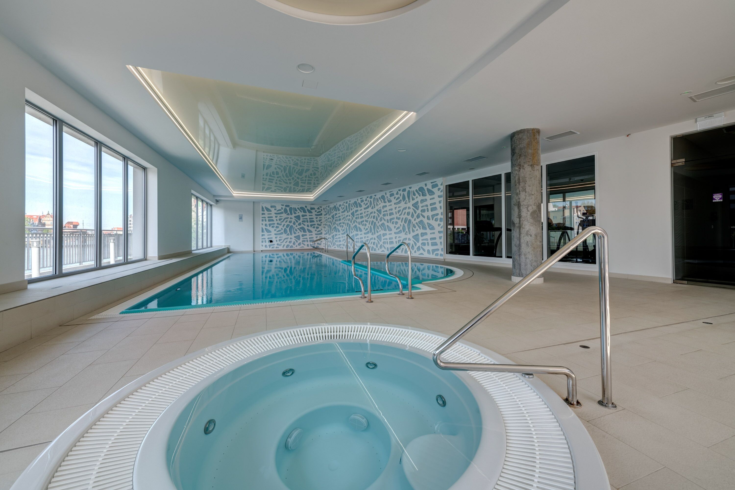 Une piscine intérieure dotée d’un jacuzzi, de grandes fenêtres et d’un design moderne au niveau du plafond.