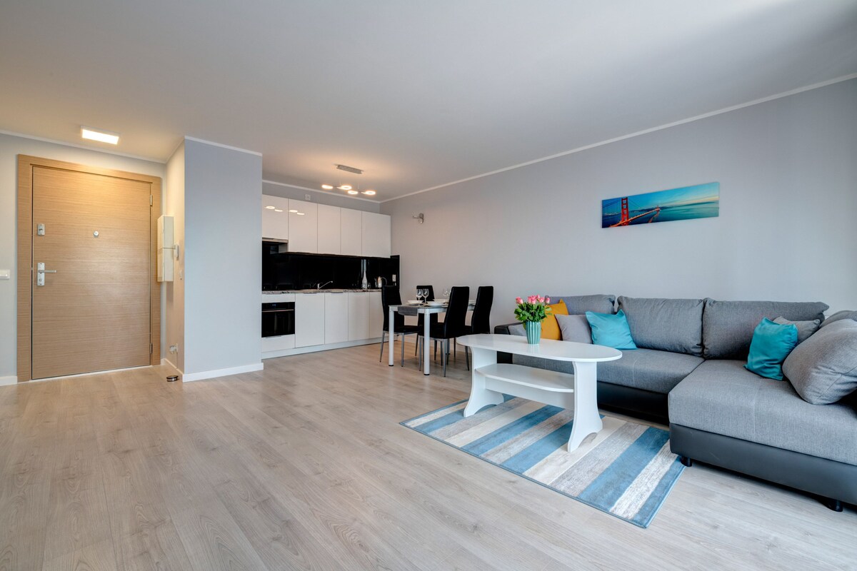 Ein modernes Wohnzimmer mit einem grauen Sofa, einem weißen Couchtisch und einem Essbereich mit Tisch und Stühlen.
