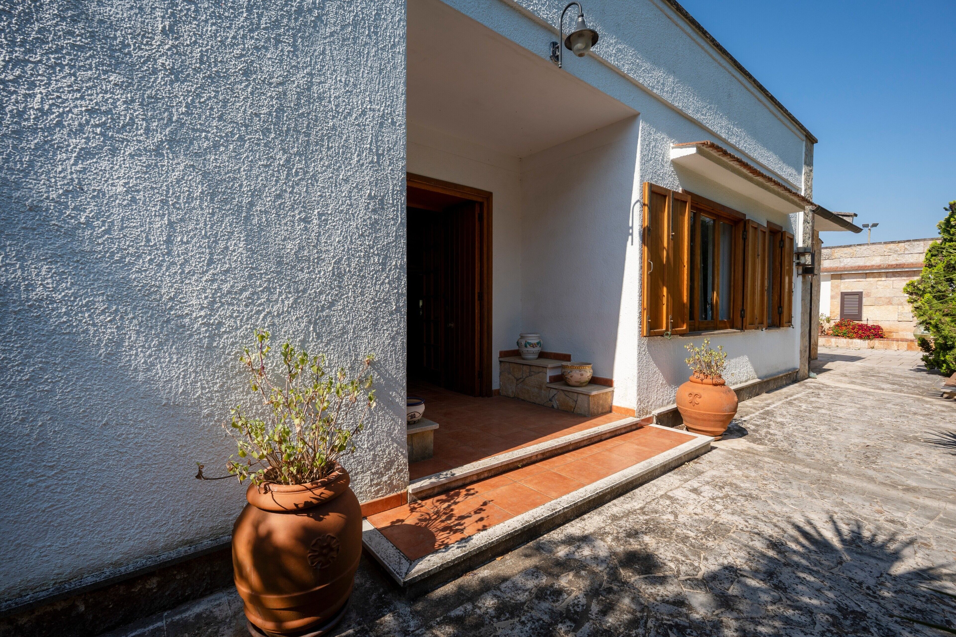 A building with a white exterior, a wooden door, and a small porch area with potted plants.