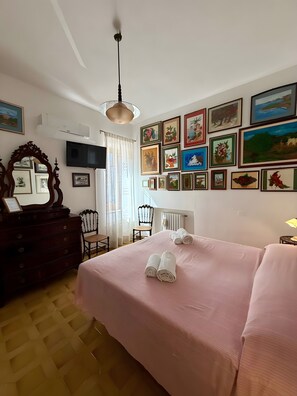 Ein Hotelzimmer mit einem Bett, einem Schminktisch, einem Sessel, einem Fernseher und einer Wand mit gerahmten Bildern.