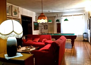 Ett vardagsrum med en röd soffa, ett biljardbord och en stor lampa.