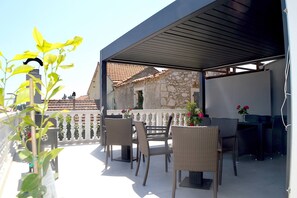 An outdoor patio with wicker furniture, a stone building in the background, and a white railing. - Groundfloor Apartment Landula (Preko)