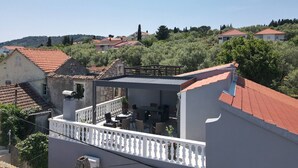 Un immeuble résidentiel doté d’un balcon, d’un toit recouvert de tuiles rouges et offrant une vue sur les maisons et la végétation environnantes.