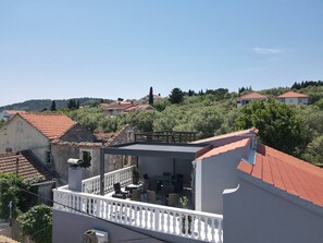A residential building with a balcony, a red-tiled roof, and a view of surrounding houses and greenery. - Groundfloor Apartment Landula (Preko)