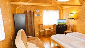 Quarto de cabana de madeira com uma cama, uma escrivaninha, uma televisão e uma cadeira.