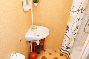 Ein Badezimmer mit Waschbecken, Toilette, Duschvorhang und einer kleinen Topfpflanze.