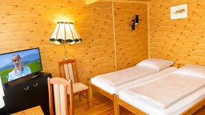 Quarto de cabana de madeira com televisão, uma cadeira, duas camas e um abajur.