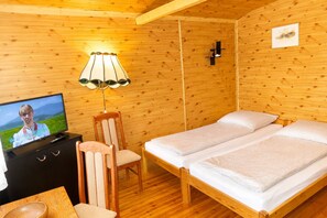 Ein Zimmer einer Holzhütte mit Fernseher, einem Sessel, zwei Betten und einer Lampe.