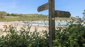 Ein hölzernes Wegweiser mit Hinweisen zum 'Coast Path Public Footpath Swansea 2m' und 'Coast Path Public Footpath Mawran Church 3m'.