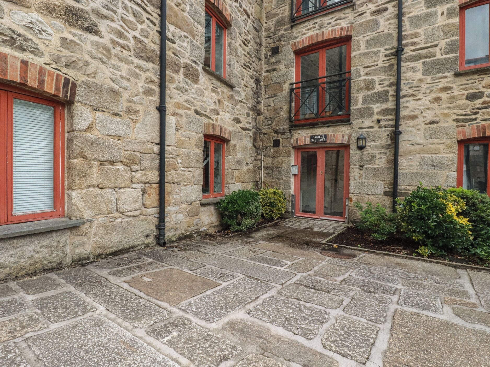 Um edifício de pedra com uma porta vermelha com a placa 'Daniel's Sail Loft'.